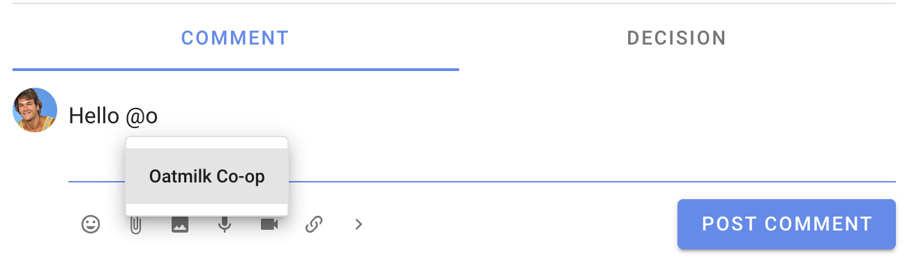 Screenshot of a comment mid-writing. The author is typing "@o" and a dropdown appears below with "Oatmilk Co-op" listed, showing they can click this to quickly mention the whole group.